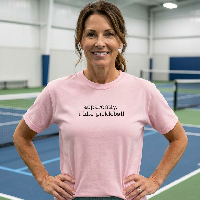 Woman wearing a pink apparently, I like pickleball t-shirt on an indoor pickleball court