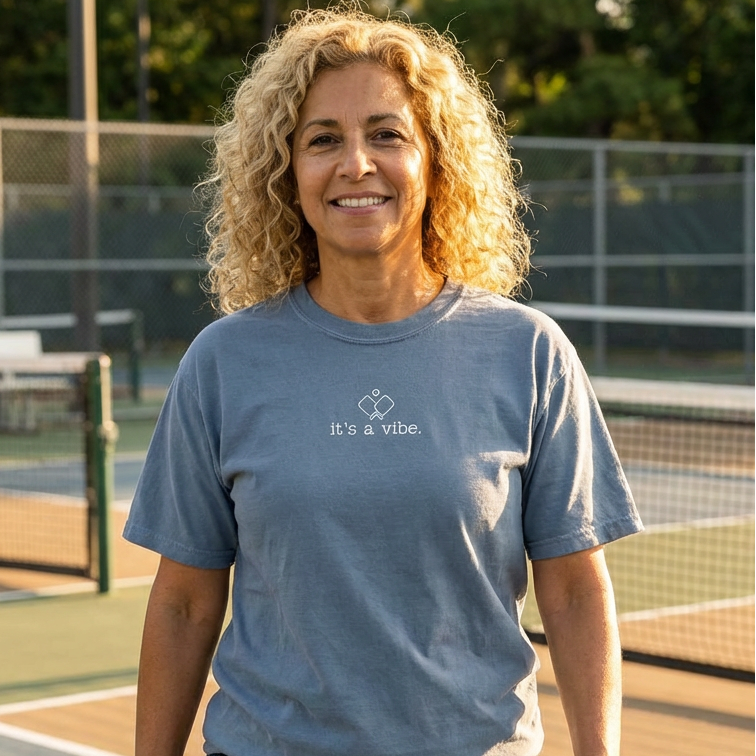 Woman wearing a blue comfort colors pickleball t-shirt that says it's a vibe on a pickleball court