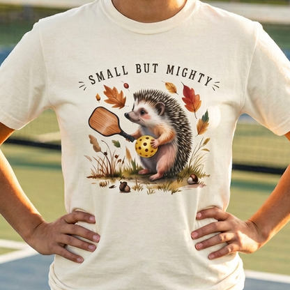 Woman wearing an ivory pickleball t-shirt with a hedgehog graphic on a pickleball court