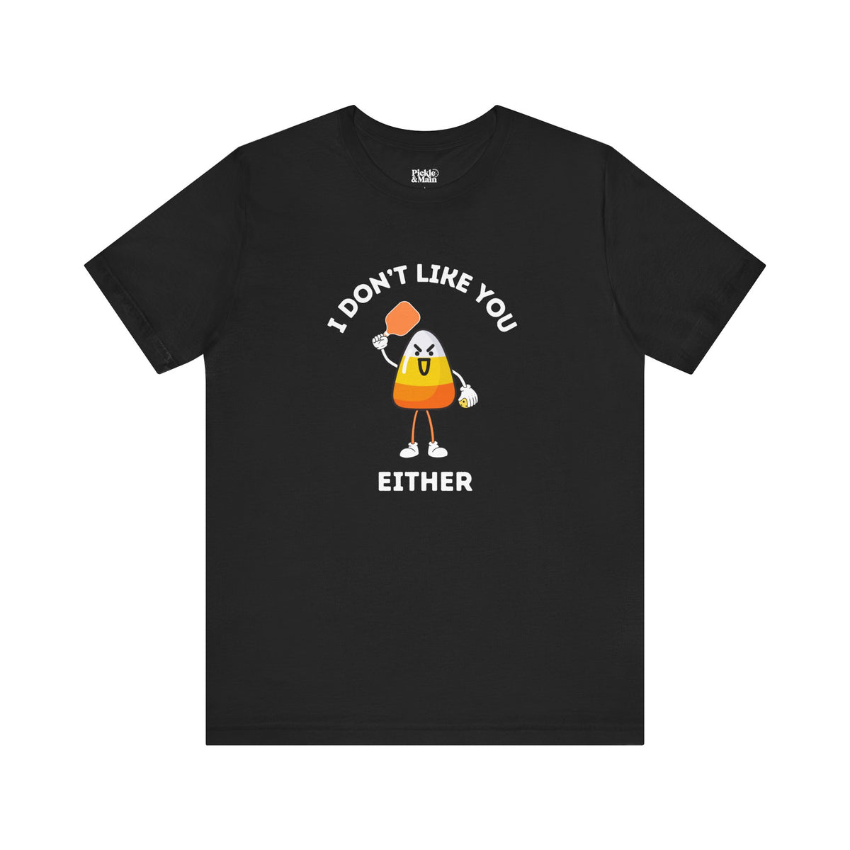 A black short-sleeve t-shirt with a graphic of a cartoon candy corn character holding a pickleball paddle and a pickleball and the text 'I DON'T LIKE YOU EITHER' printed on the front, displayed against a solid white background.