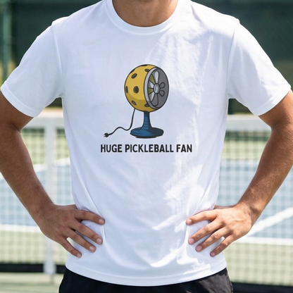 A man standing on a pickleball court wearing a white graphic t-shirt with a yellow pickleball fan design and the text 'HUGE PICKLEBALL FAN'.