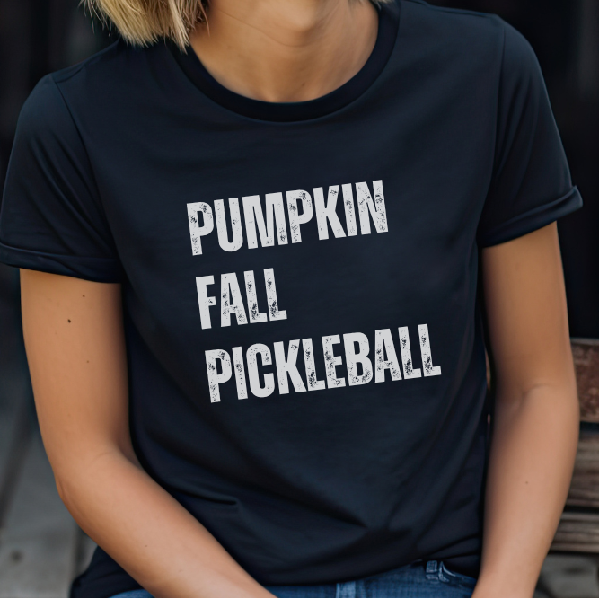 A person wearing a dark navy blue t-shirt with the words 'PUMPKIN FALL PICKLEBALL' printed in distressed white block letters across the chest.