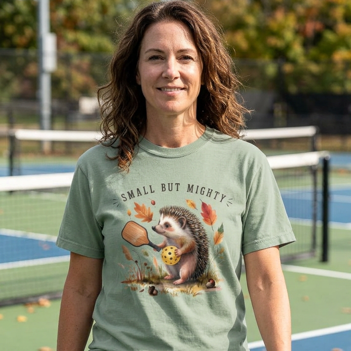 Woman wearing a green pickleball t-shirt with a hedgehog graphic on a pickleball court