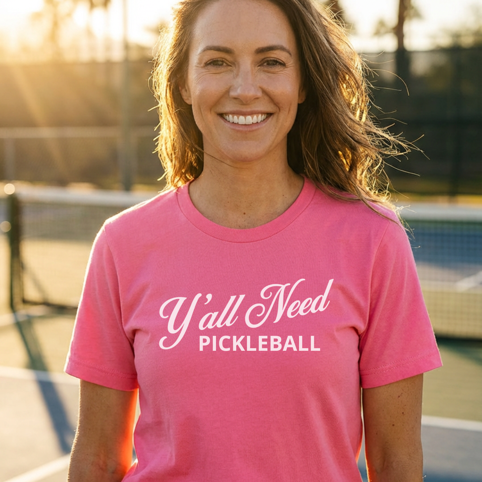 Woman wearing a pink t-shirt with 'Y'all Need Pickleball' text on a pickleball court