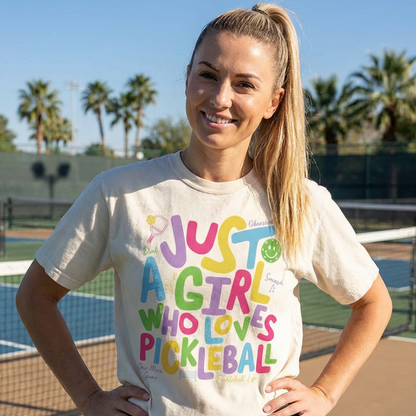 Woman wearing a colorful 'Just a Girl Who Loves Pickleball' shirt on a tennis court.