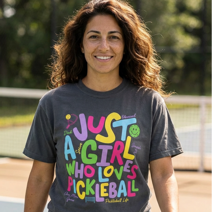 Woman wearing a pickleball t-shirt with colorful text that says just a girl who loves pickleball 
